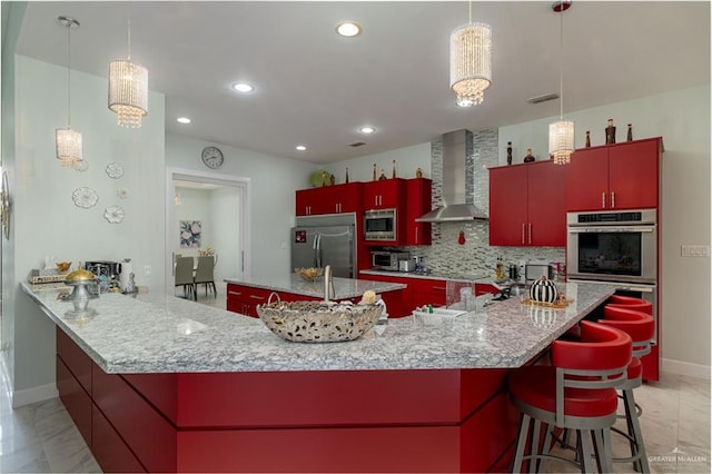 kitchen featuring wall chimney range hood, built in appliances, kitchen peninsula, pendant lighting, and decorative backsplash