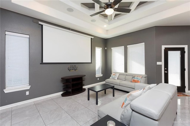 home theater with a tray ceiling, ceiling fan, baseboards, and light tile patterned floors