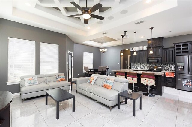 living room with light tile patterned floors, visible vents, coffered ceiling, a tray ceiling, and ceiling fan with notable chandelier