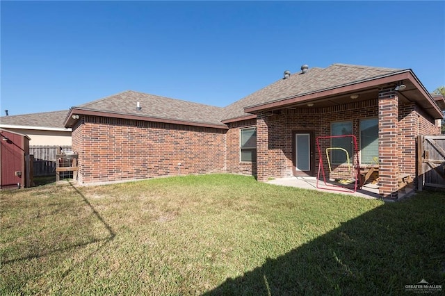 rear view of house with a shingled roof, fence, a lawn, and brick siding