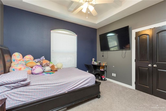 carpeted bedroom with a tray ceiling, ceiling fan, and baseboards