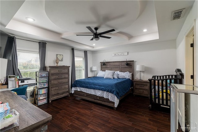 bedroom featuring a raised ceiling, visible vents, multiple windows, and wood finished floors