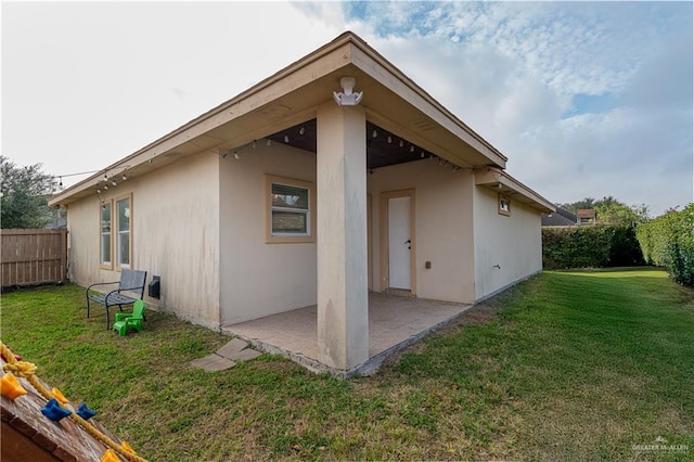 rear view of house with stucco siding, fence, a patio, and a yard