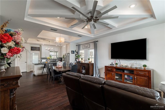 living area with ceiling fan with notable chandelier, a tray ceiling, dark wood-style flooring, and visible vents