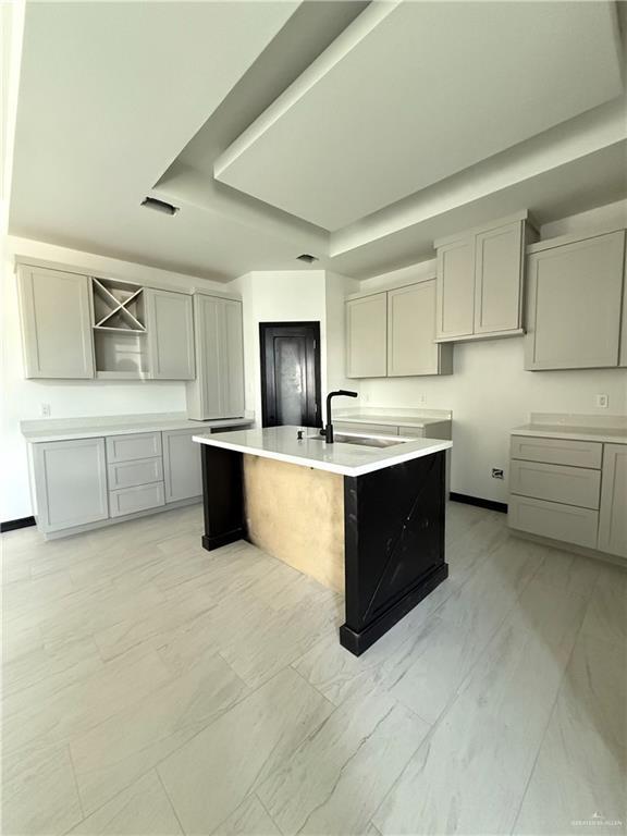 204 S 83rd St, Edinburg, TX 78542 - kitchen featuring a sink, a tray ceiling, gray cabinets, an island with sink, and light marble finish floors
