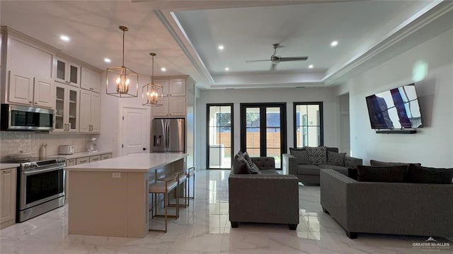 kitchen with a center island, stainless steel appliances, a kitchen breakfast bar, decorative light fixtures, and a tray ceiling