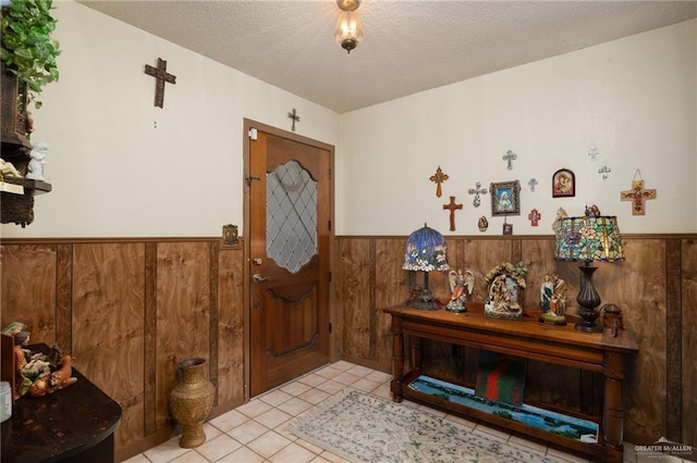 foyer entrance with wooden walls, a textured ceiling, and light tile patterned flooring