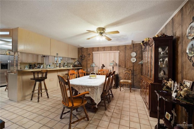 tiled dining room featuring a textured ceiling, ceiling fan, and wood walls