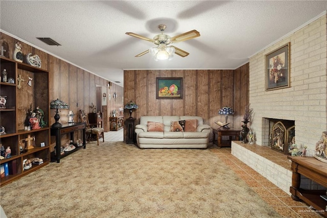 carpeted living room featuring ceiling fan, wooden walls, ornamental molding, a textured ceiling, and a brick fireplace