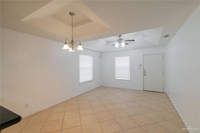 tiled empty room featuring a tray ceiling and ceiling fan with notable chandelier