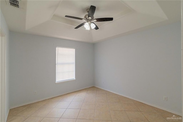 tiled empty room featuring ceiling fan and a raised ceiling