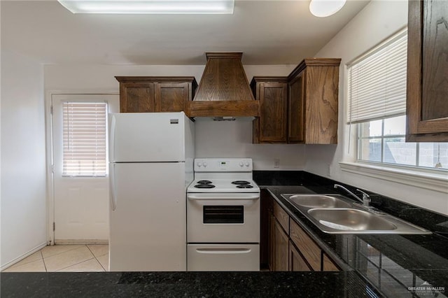 kitchen featuring sink, dark stone countertops, custom exhaust hood, light tile patterned floors, and white appliances