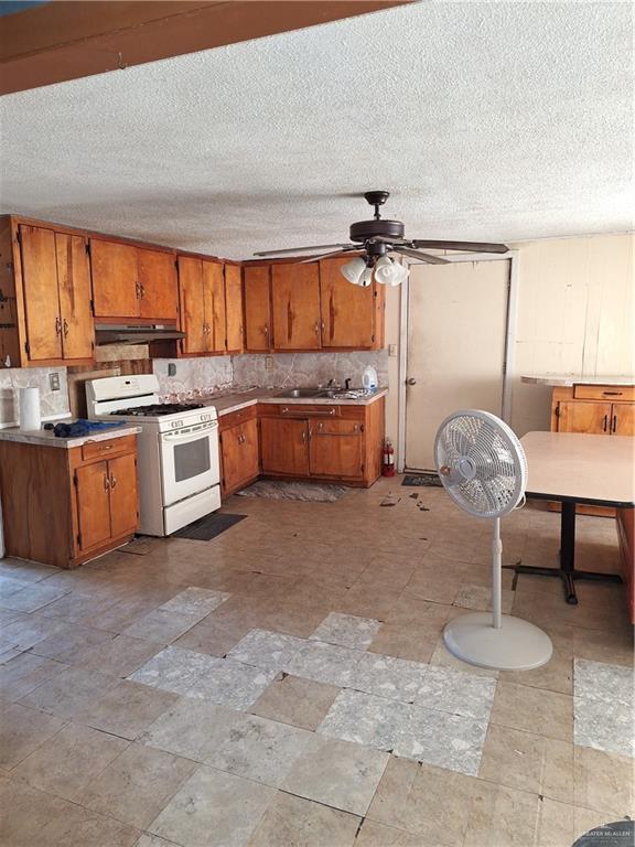 2044 Balboa Ave, Mcallen, TX 78503 - kitchen with white range with gas stovetop, under cabinet range hood, brown cabinetry, ceiling fan, and a sink