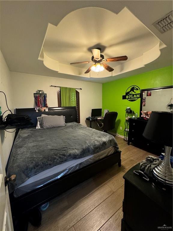 bedroom with a tray ceiling, ceiling fan, and hardwood / wood-style flooring