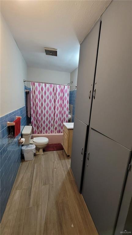 full bathroom featuring tile walls, hardwood / wood-style floors, vanity, toilet, and shower / bath combo with shower curtain