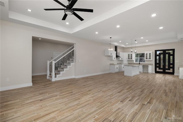 unfurnished living room with a raised ceiling, ceiling fan, and light hardwood / wood-style floors