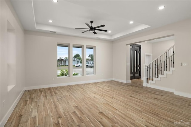 unfurnished living room featuring ceiling fan, light hardwood / wood-style floors, and a raised ceiling