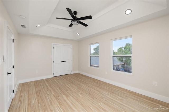 unfurnished bedroom featuring light wood-type flooring, a closet, a raised ceiling, and ceiling fan