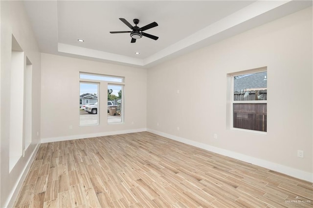 empty room with a tray ceiling, ceiling fan, and light hardwood / wood-style flooring