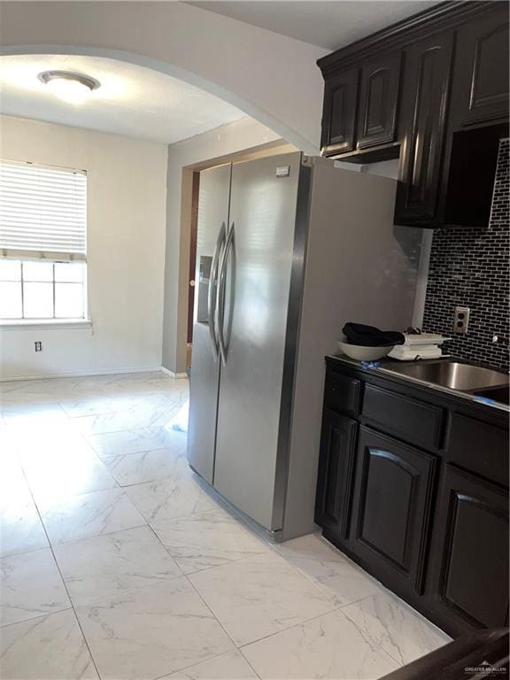 kitchen with stainless steel fridge, tasteful backsplash, arched walkways, marble finish floor, and a sink