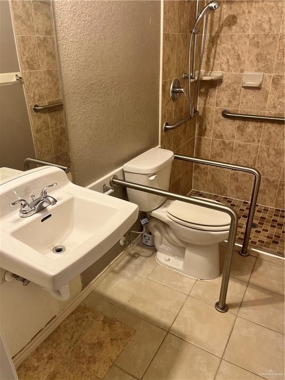 bathroom with a textured wall, toilet, a sink, a shower stall, and tile patterned floors