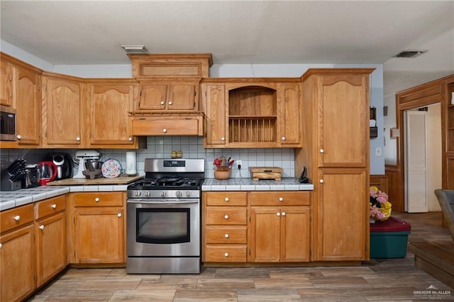 kitchen with backsplash, tile counters, stainless steel appliances, and exhaust hood