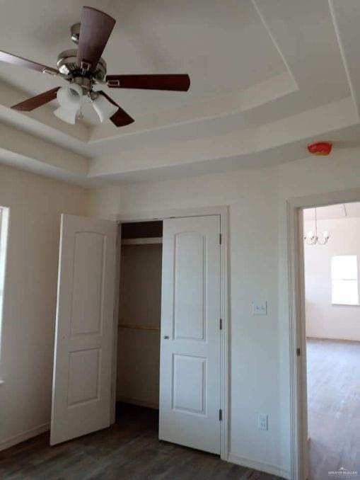 unfurnished bedroom with ceiling fan with notable chandelier, dark hardwood / wood-style floors, and a raised ceiling