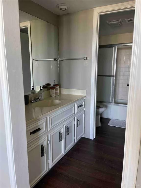 full bathroom with toilet, hardwood / wood-style flooring, bath / shower combo with glass door, and vanity