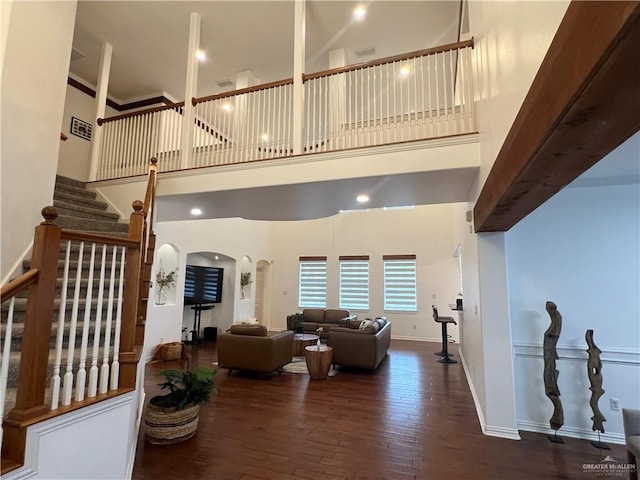 living room featuring hardwood / wood-style flooring, a high ceiling, arched walkways, and stairway