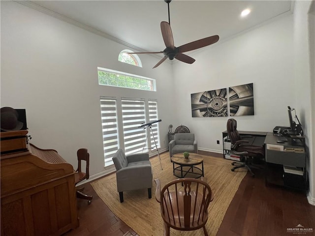 office area with a towering ceiling, wood finished floors, ornamental molding, baseboards, and ceiling fan