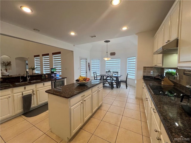 kitchen with a sink, decorative backsplash, black electric stovetop, under cabinet range hood, and visible vents
