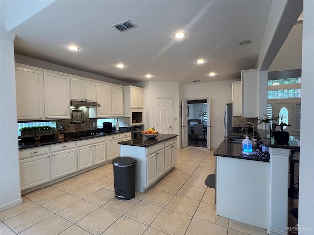 kitchen featuring a sink, oven, backsplash, under cabinet range hood, and a kitchen island
