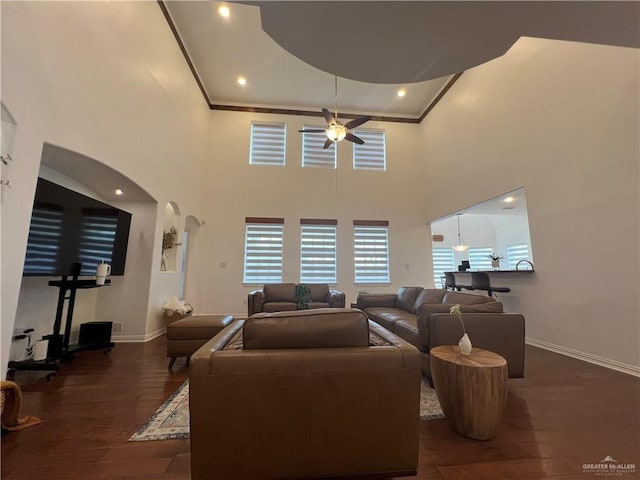 living room featuring arched walkways, dark wood finished floors, baseboards, a ceiling fan, and crown molding