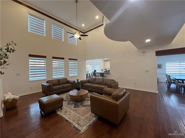 living room with a towering ceiling, baseboards, a ceiling fan, dark wood-type flooring, and ornamental molding
