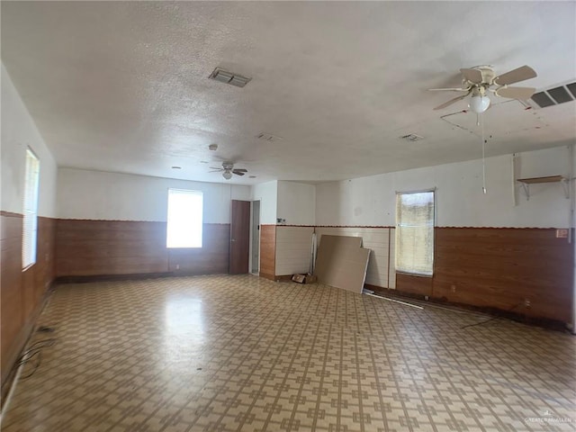 unfurnished room with ceiling fan, wooden walls, and a textured ceiling