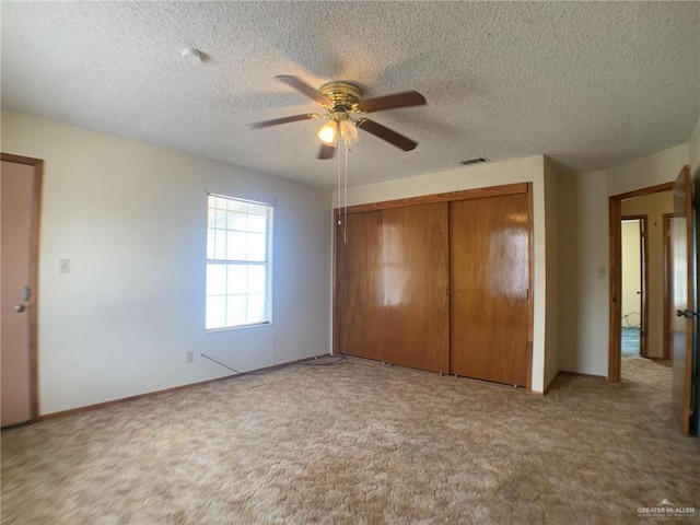 unfurnished bedroom with ceiling fan, light carpet, a textured ceiling, and a closet