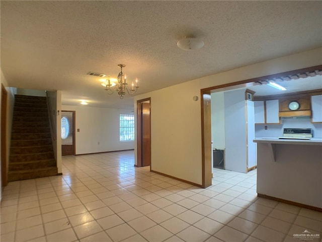 tiled empty room with a textured ceiling and a chandelier