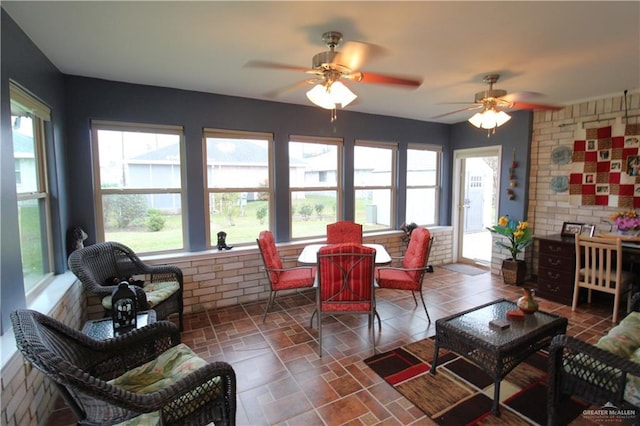 living room featuring ceiling fan, plenty of natural light, and brick wall