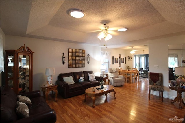 living room featuring ceiling fan, wood-type flooring, and a raised ceiling