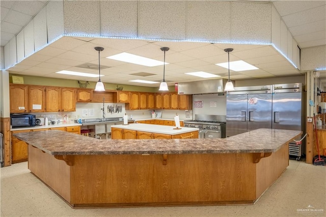 kitchen with pendant lighting, premium appliances, a drop ceiling, and a spacious island