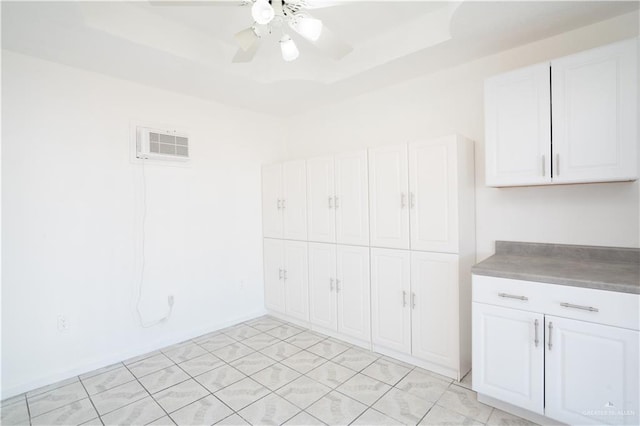 interior space featuring a raised ceiling, white cabinetry, and ceiling fan