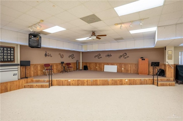 interior space featuring a paneled ceiling, wooden walls, ceiling fan, and track lighting