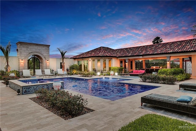 pool at dusk with outdoor lounge area, a patio area, and an in ground hot tub