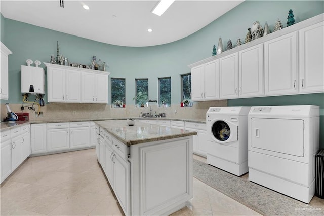 washroom featuring washing machine and clothes dryer, sink, tankless water heater, cabinets, and light tile patterned floors