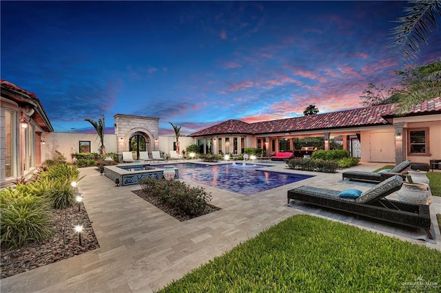 pool at dusk with an in ground hot tub and a patio area