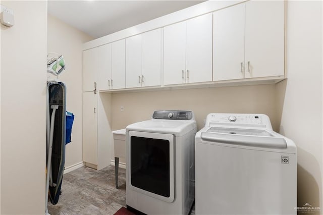 clothes washing area with cabinets, washing machine and clothes dryer, and light hardwood / wood-style floors