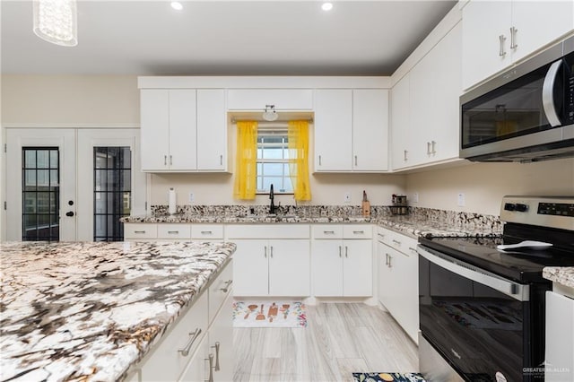 kitchen with stainless steel appliances, light stone countertops, french doors, and white cabinetry