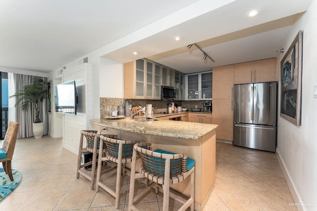 kitchen featuring light stone countertops, a sink, stainless steel appliances, a peninsula, and glass insert cabinets