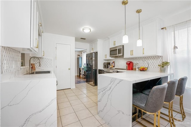 kitchen with pendant lighting, sink, appliances with stainless steel finishes, tasteful backsplash, and white cabinetry