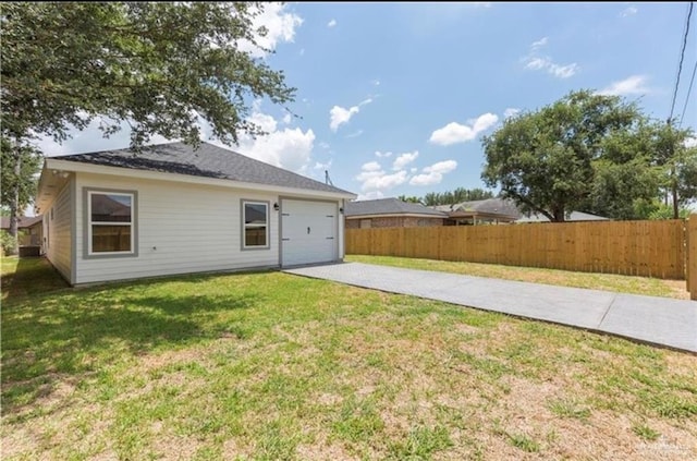 rear view of property with a lawn, fence, driveway, and a garage